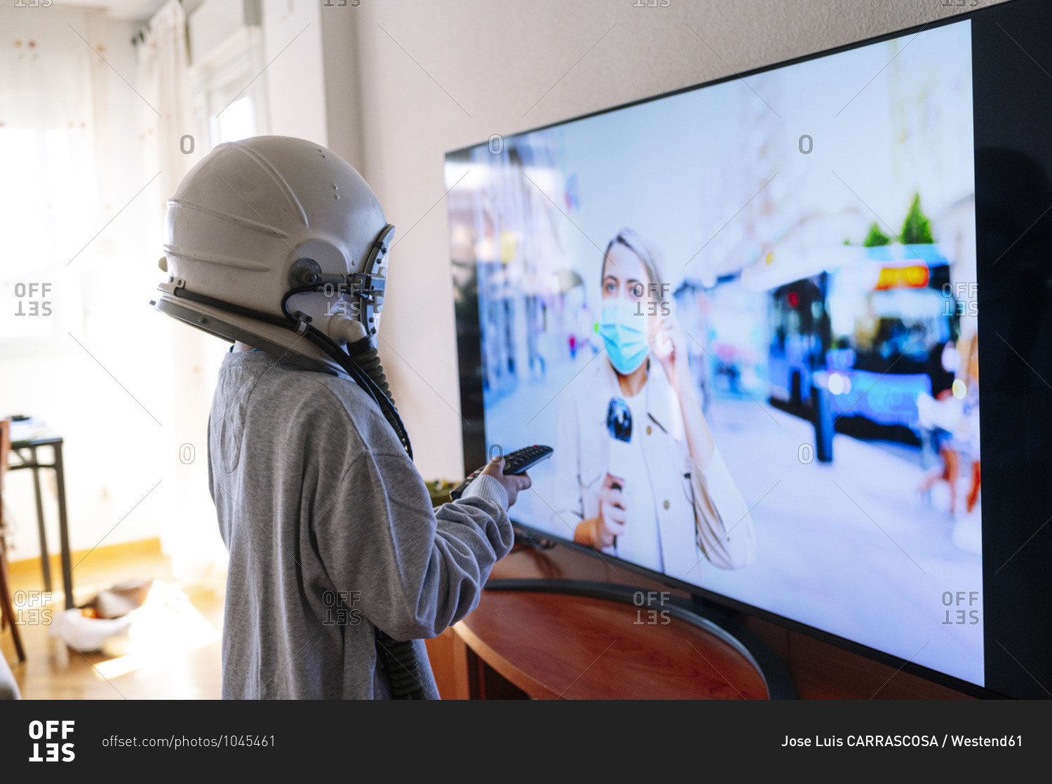 Boy wearing space helmet watching journalist mother on TV while standing at home