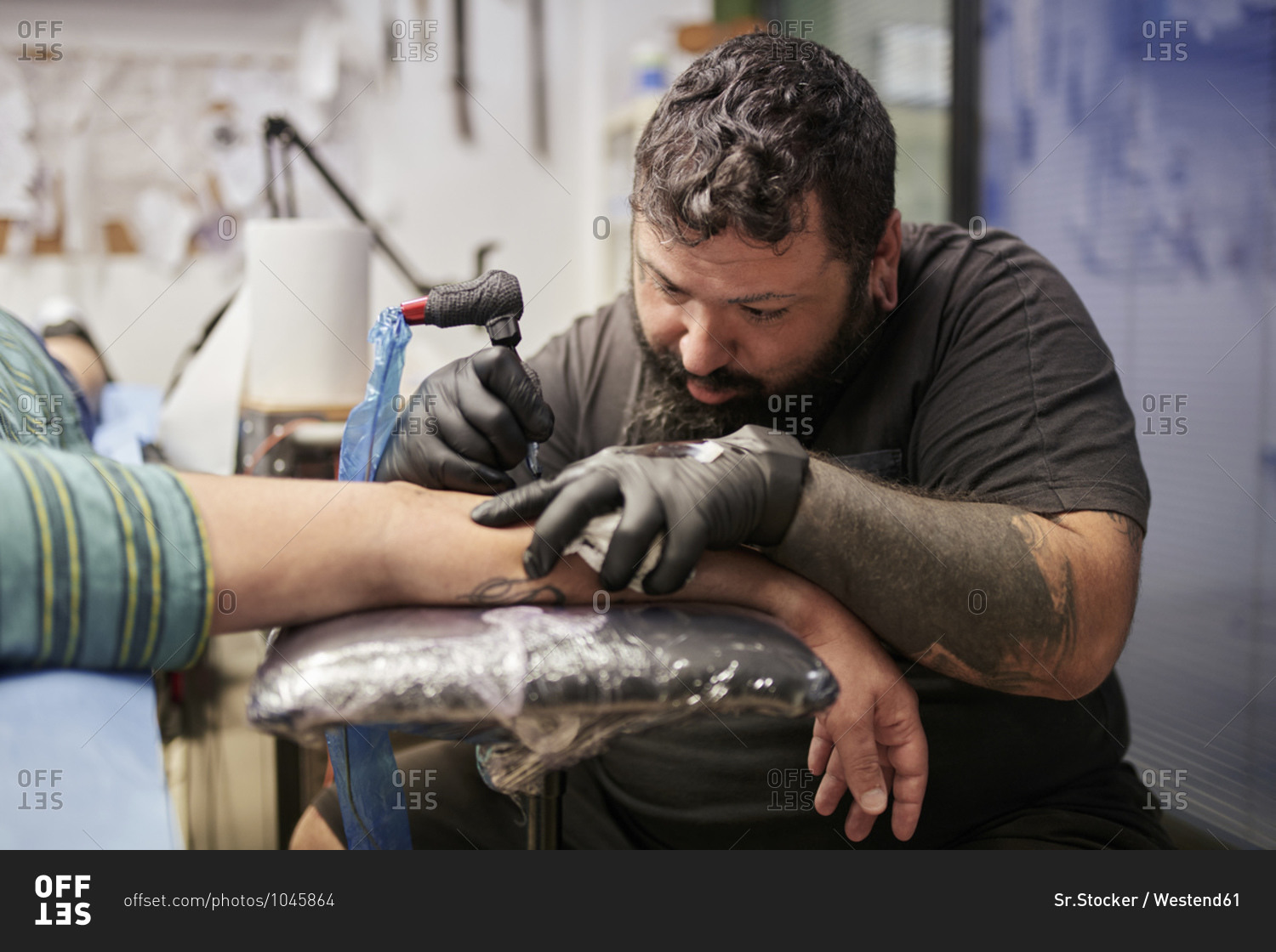 Bearded artist tattooing on male customer\'s hand in studio