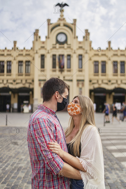 Couple with protective face mask embracing on street in city