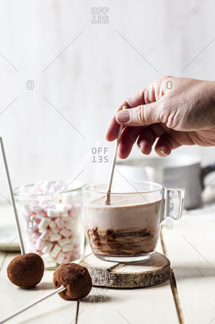 Hand of woman mixing hot chocolate by truffle lollipops and marshmallows on table at home