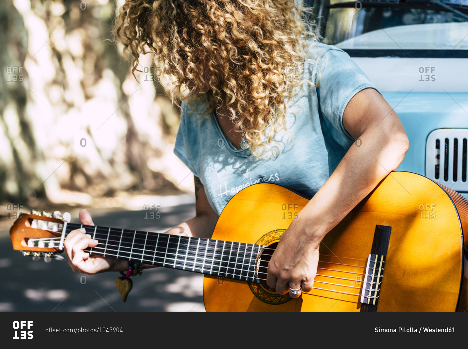 Mature woman with curly hair playing guitar while leaning on motor home