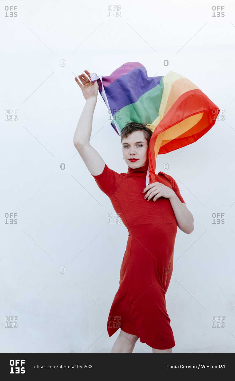 Non-Binary person waving rainbow flag while standing against white background