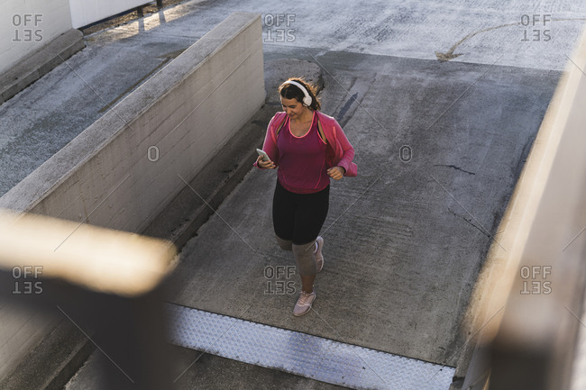 Young woman using mobile phone while running on terrace at sunset