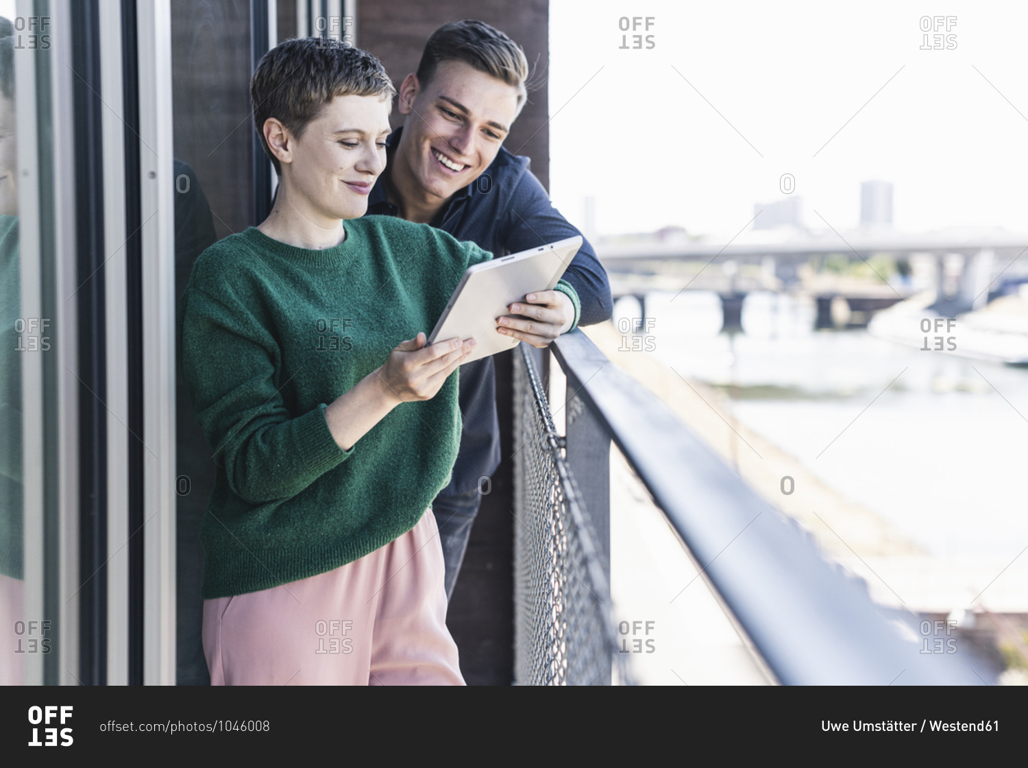 Smiling colleagues discussing over digital tablet while standing in balcony at office