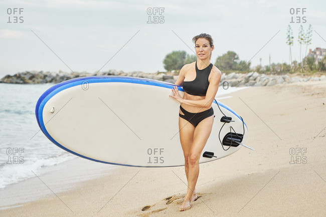 Smiling woman walking while carrying surfboard on beach during sunset