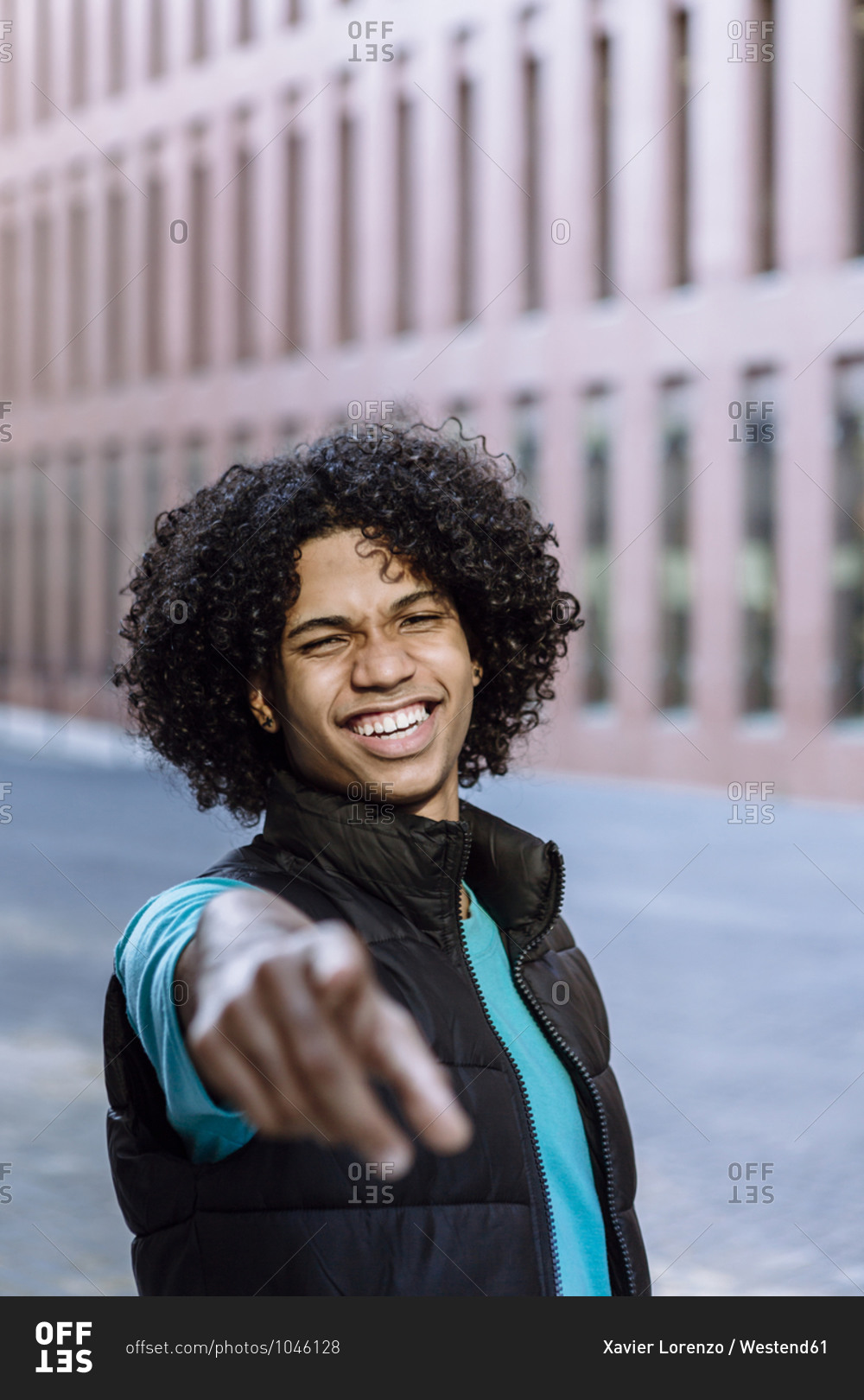 Happy young man pointing while standing on street in city