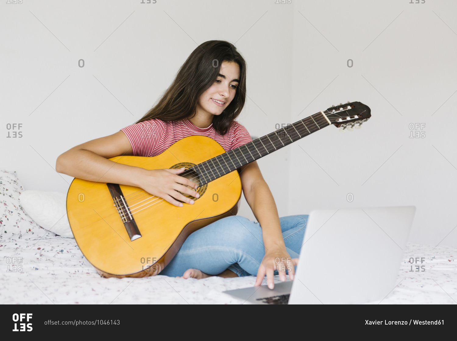 Woman learning guitar online at home in bedroom