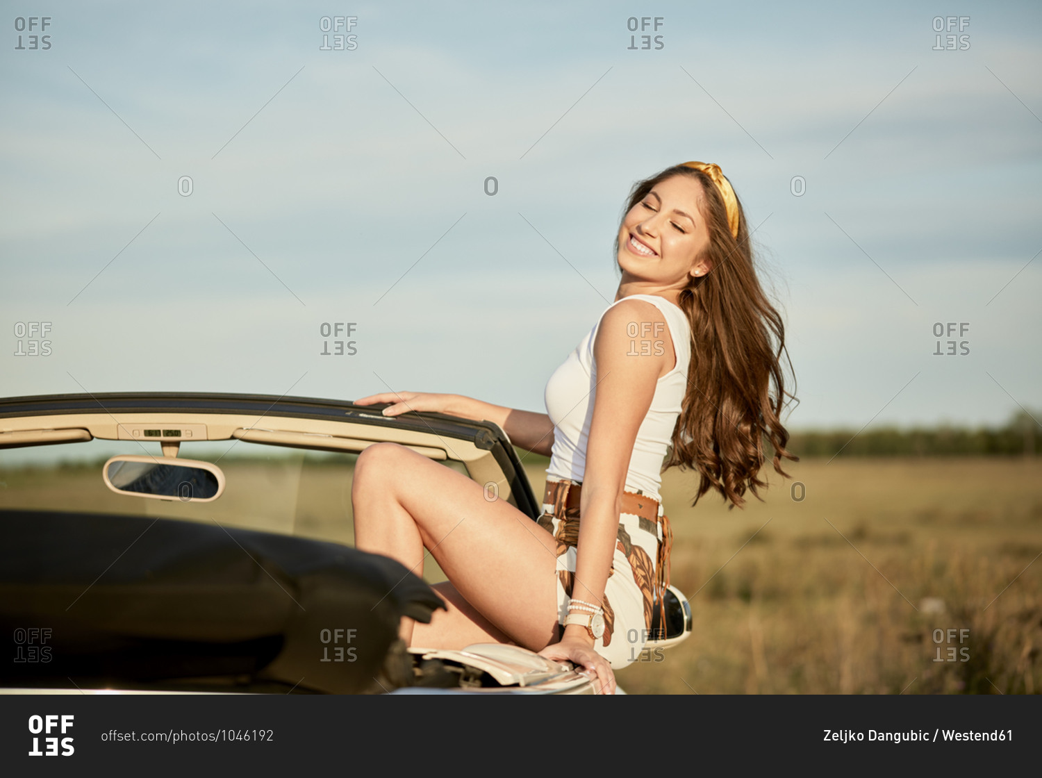 Smiling woman with long hair sitting on luxury car