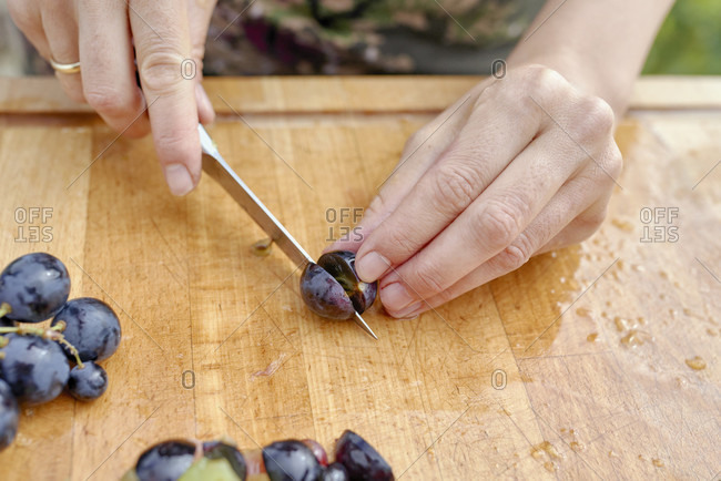 Women's hands with a kitchen knife stone grapes