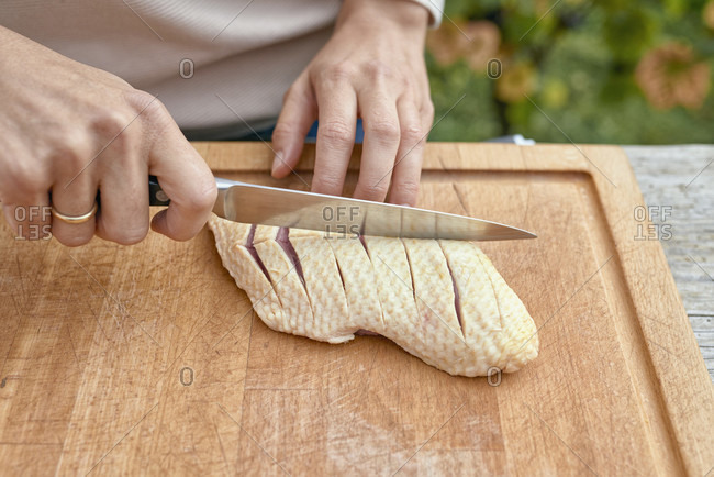 Woman's hands with chef's knife carve the skin of a duck breast on a wooden board