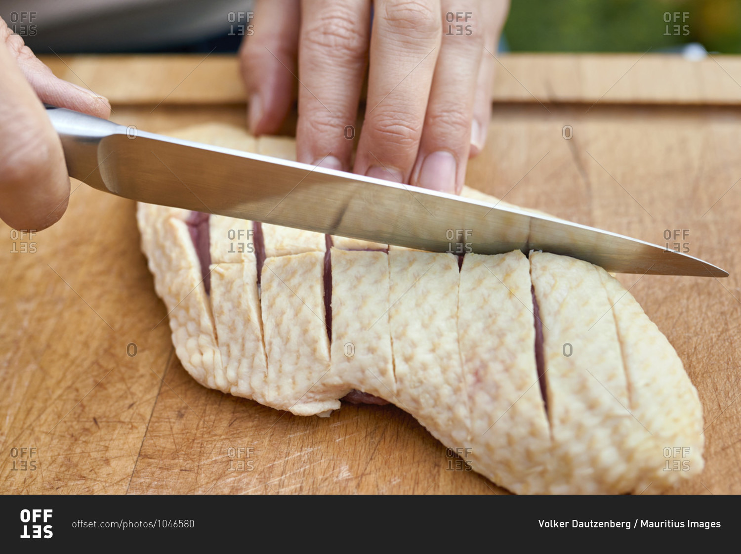Woman\'s hands with chef\'s knife carve the skin of a duck breast on a wooden board