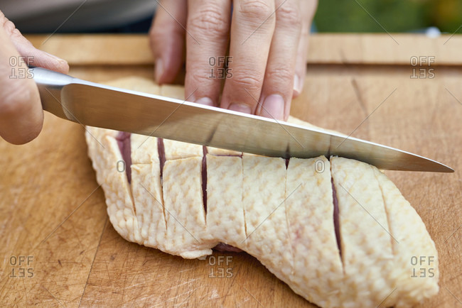 Woman's hands with chef's knife carve the skin of a duck breast on a wooden board