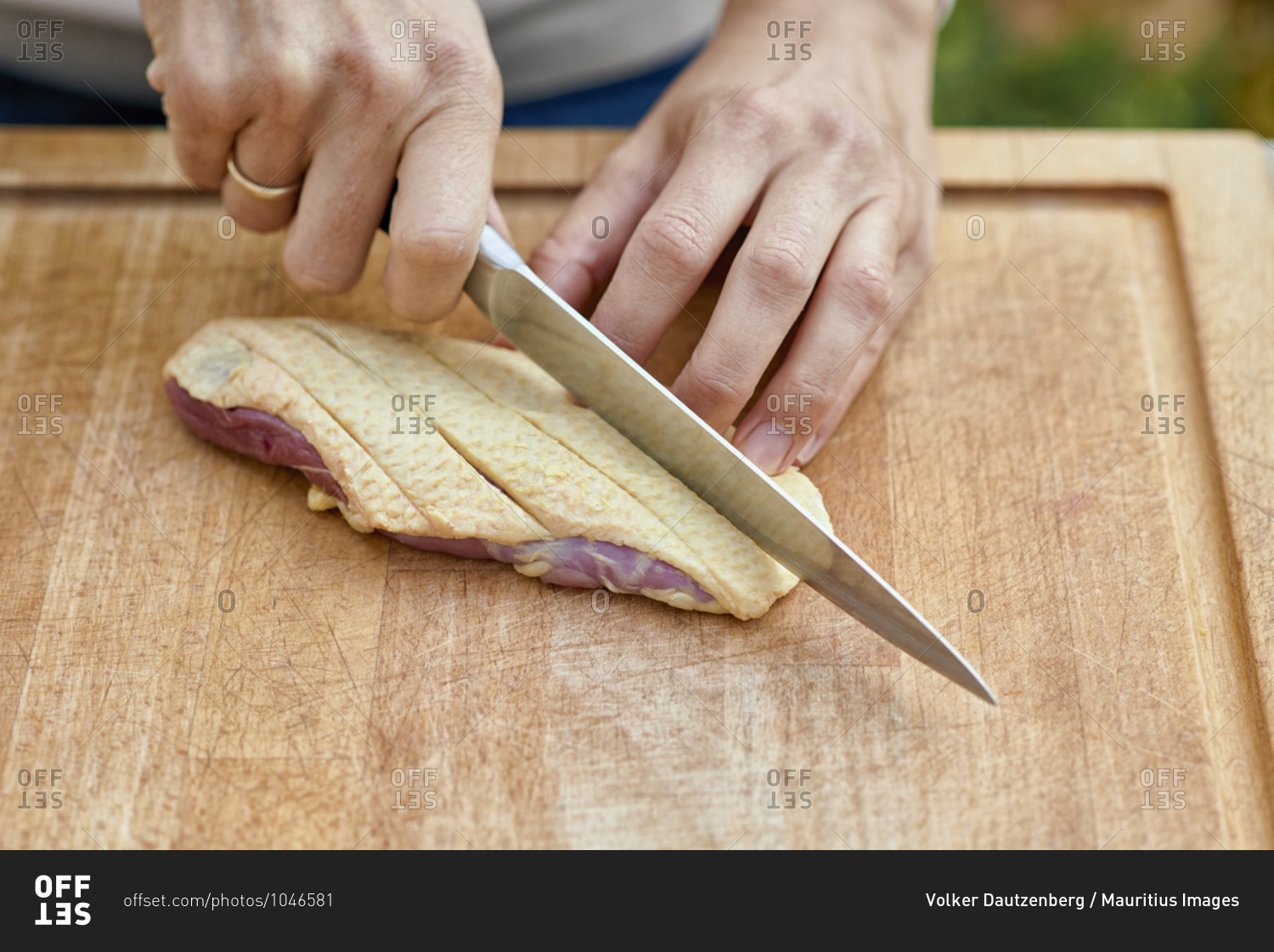 Woman\'s hands with chef\'s knife carve the skin of a duck breast on a wooden board