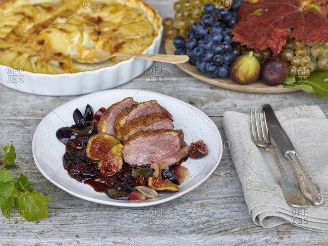 Duck breast with grape-fig sauce, gratin of potatoes, pumpkin and jerusalem artichokes, grapes and figs, silver cutlery, table with untreated table top