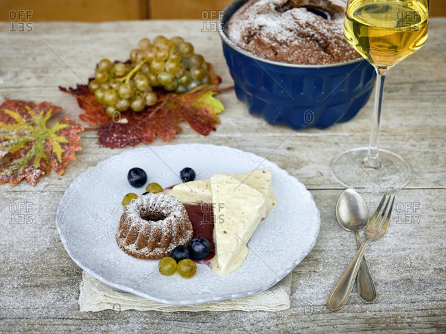 Sweet wine parfait with a small guglhupf and wine berries on a white plate, white wine glass filled and baking pan, table with untreated table top