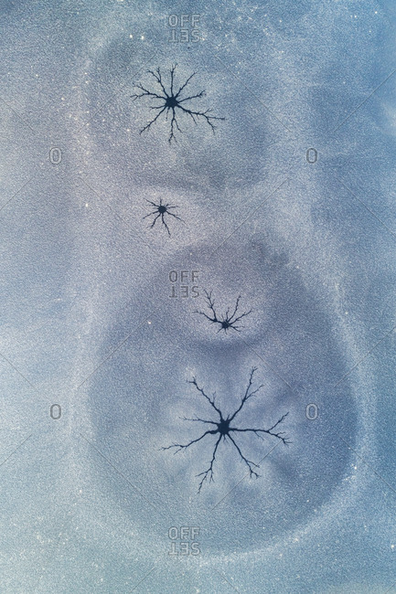 Abstract aerial view of thin layer of ice with cracks and some snow on a small lake after a night of frost, embedded like in a matryoshka, Twente, Overijssel, Netherlands