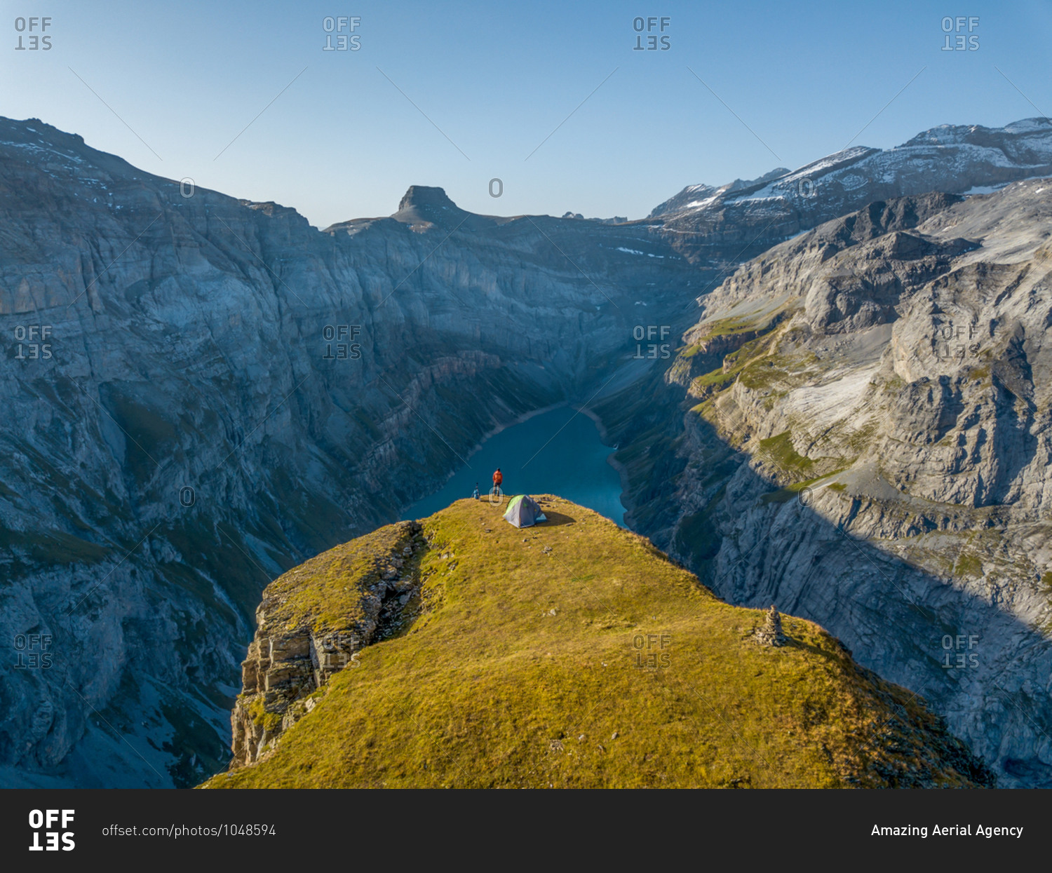 Aerial View of hiker with tent admiring view od Swiss Mountain Lake in Glarus, Switzerland.