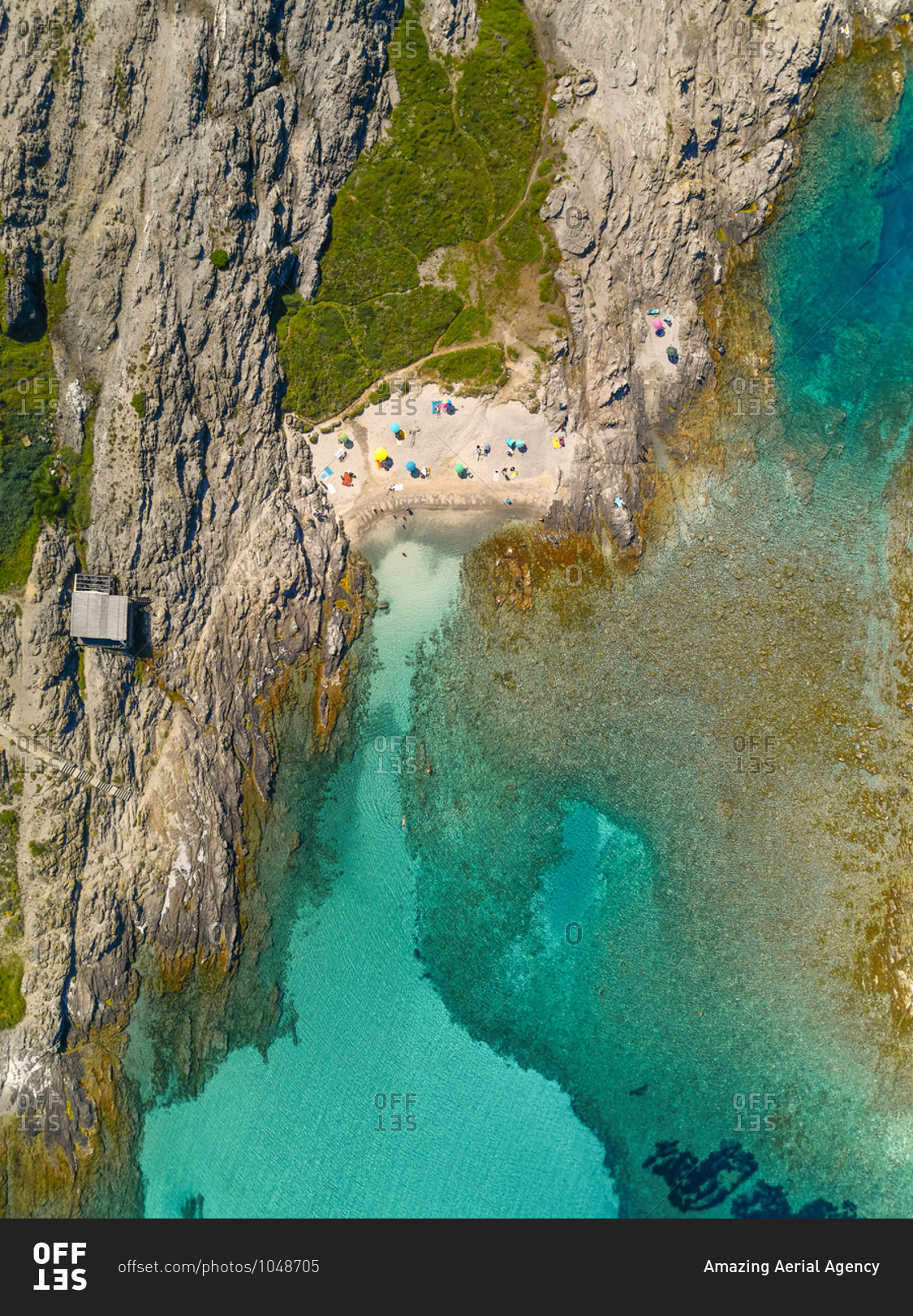 Aerial view of an amazing beach in front of a little cove with turquoise waters and many colorful parasols in Stintino, Sardinia, Italy.