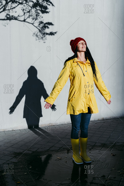 Woman wearing raincoat standing on rain puddle against shadow wall