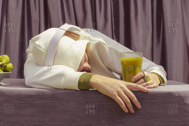 Woman with green juice listening music over headphones while lying on table at home