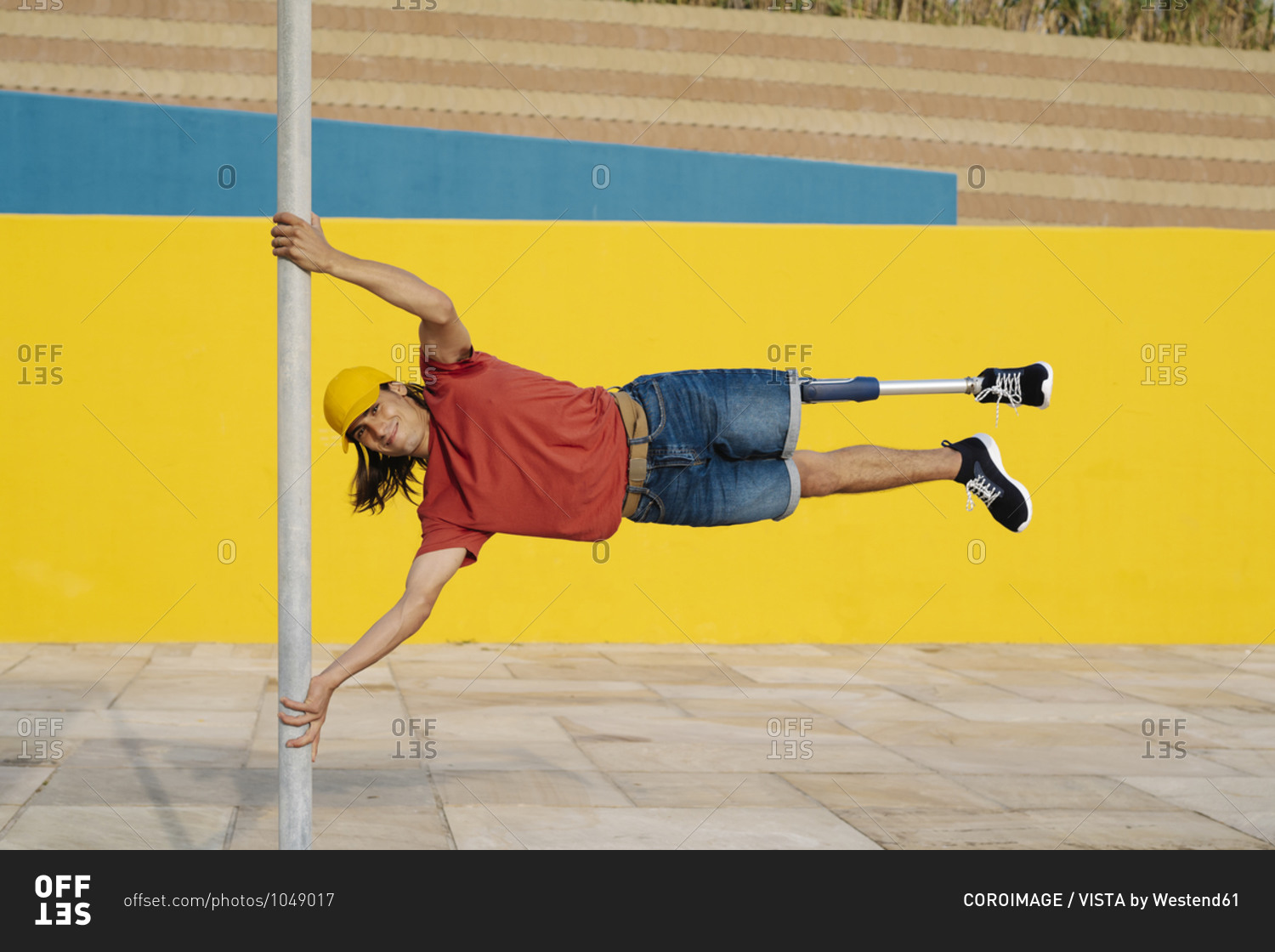 Athlete holding pole while balancing body weight against multi colored wall