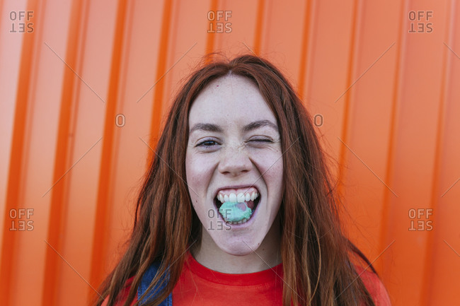 Young woman chewing gum while standing against orange wall