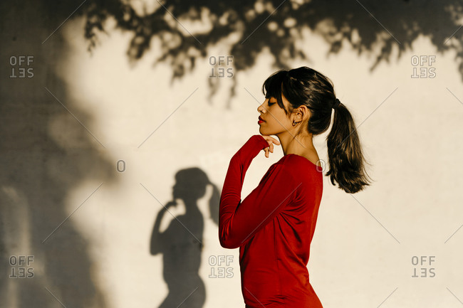 Young woman standing with hand on chin by tree shadow during sunset