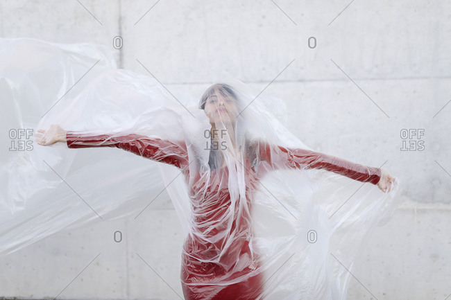 Young woman wearing red dress wrapped inside plastic against concrete wall