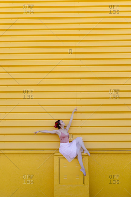 Ballerina with arms raised dancing on seat against yellow wall