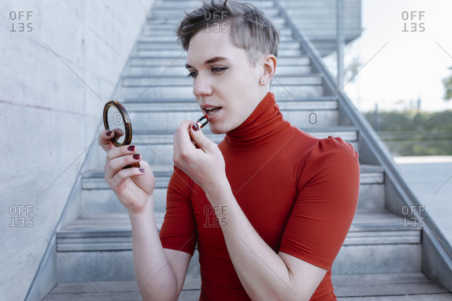 Close-up of trans young man applying lipstick while sitting on steps