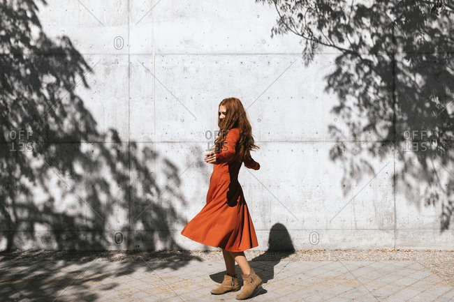 Young woman with arms outstretched spinning against tree shadow wall
