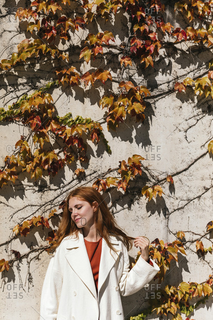 Young woman wearing jacket standing against ivy wall