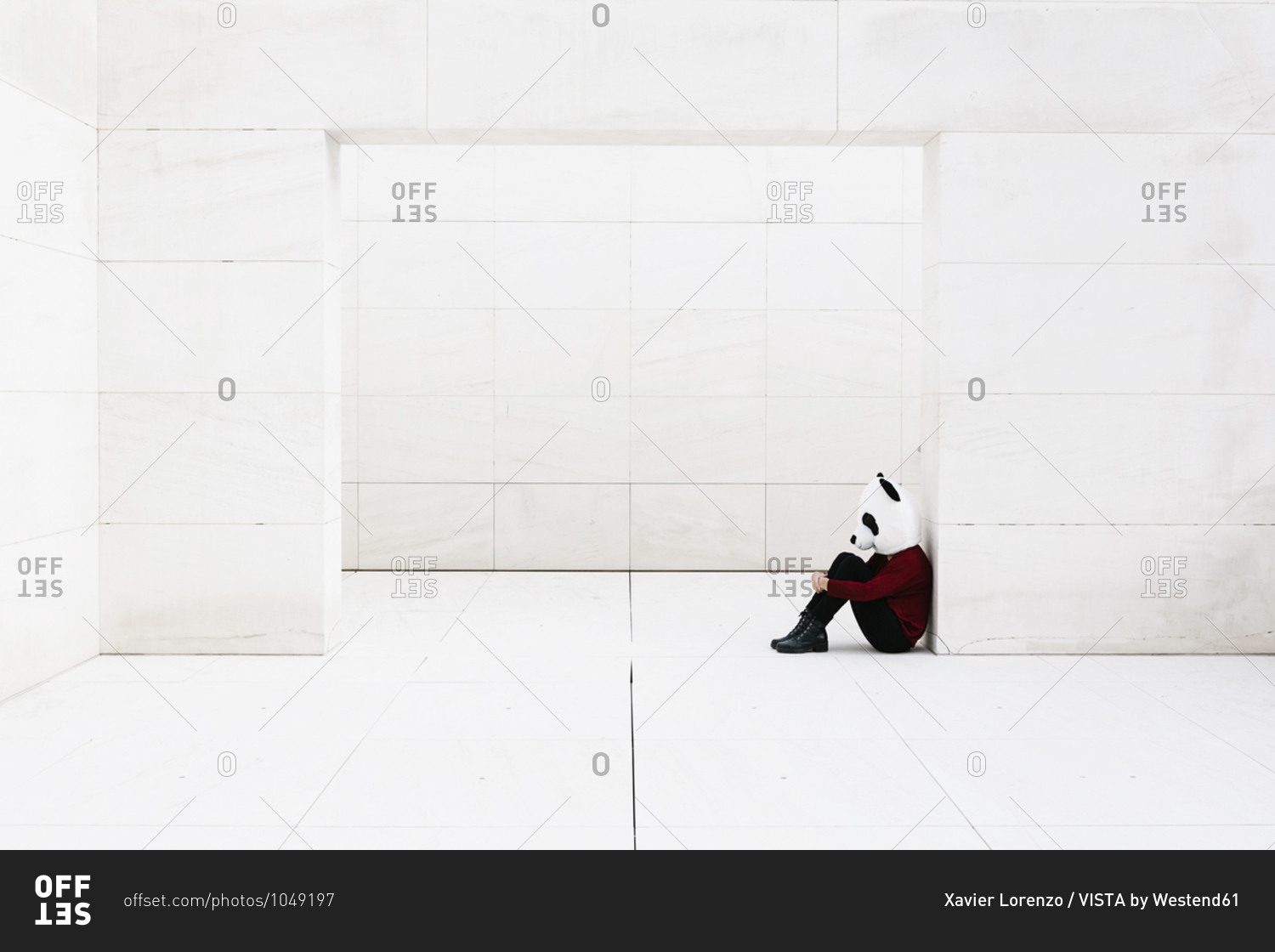 Depressed woman wearing panda mask sitting at doorway against white wall