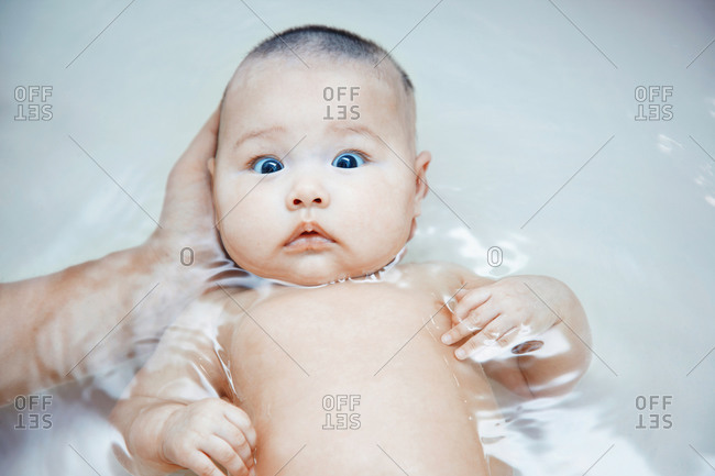 Little afraid baby in the bath supporting by the hand of father