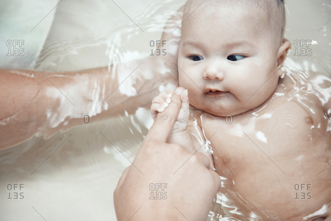 Cute baby in the bath holding finger of the father