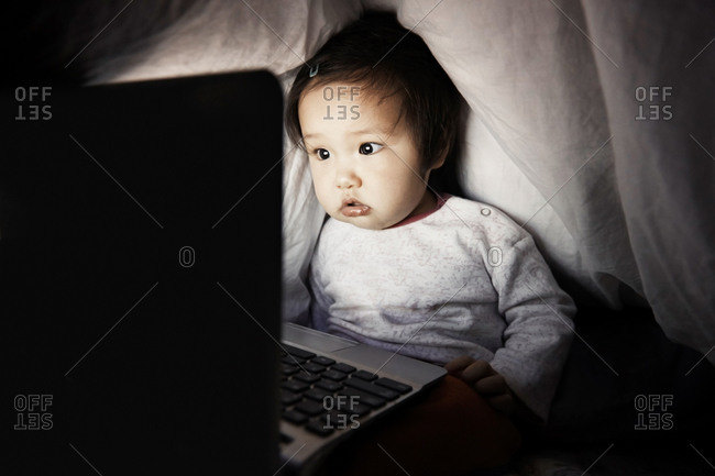 Baby girl using laptop undeneath cover