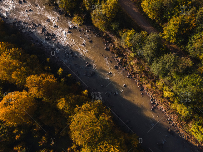 River running though color changing autumn forest viewed from above