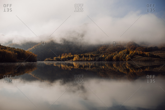 Dense fog over mountain and fall forest reflecting in a lake
