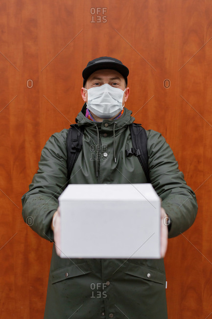 A courier wearing protective gloves and a mask holds out a parcel holding it in his hands in Penza, Russia