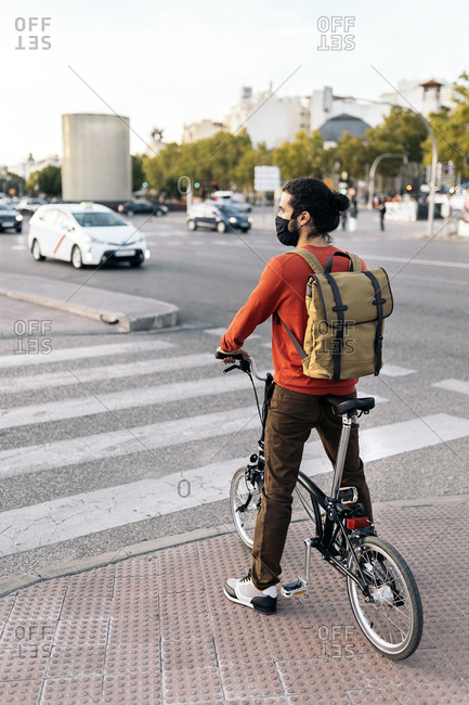 man wearing face mask waiting in a zebra crossing with his detachable bike.