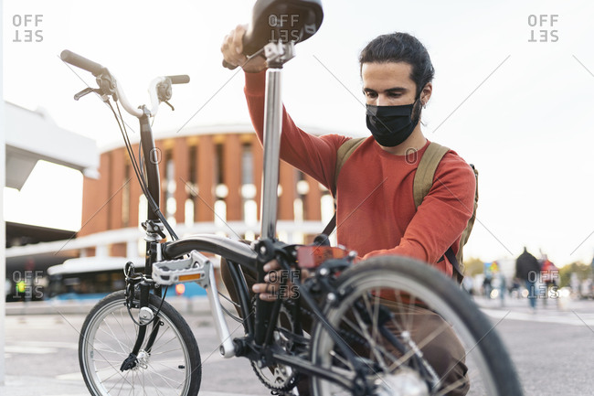 Stock photo of man wearing face mask folding his bike in the street.