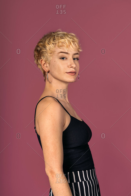 Stock photo of expressive girl wearing black tank top standing and looking at camera over pink background.