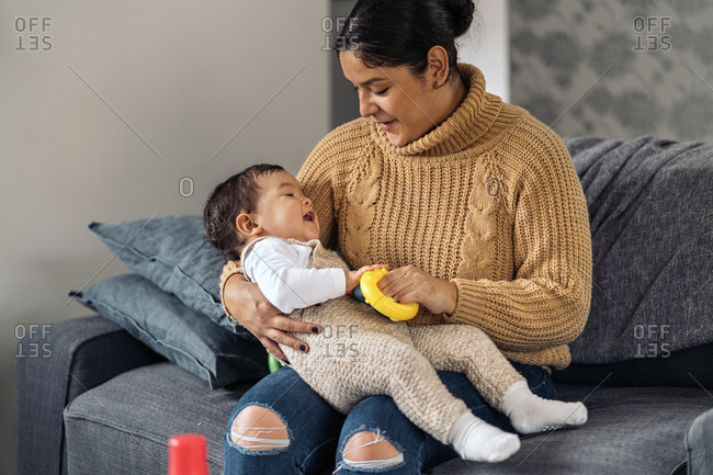 smiley woman holding her little baby while sitting in the sofa.