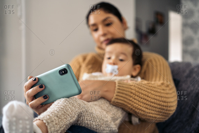 Stock photo of happy mother and her baby watching cartoons in the phone at home.