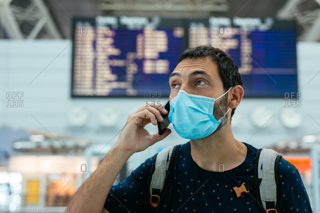 Young man wearing a face mask talking on the phone at the airport