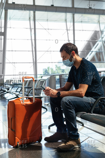Young man wearing a face mask looking at his phone at the airport