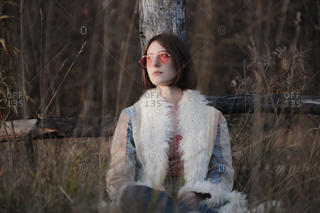 Young woman in hippie coat and red sunglasses among weeds and gr
