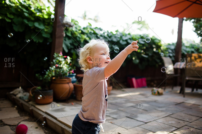 Two year old boy popping bubbles in yard