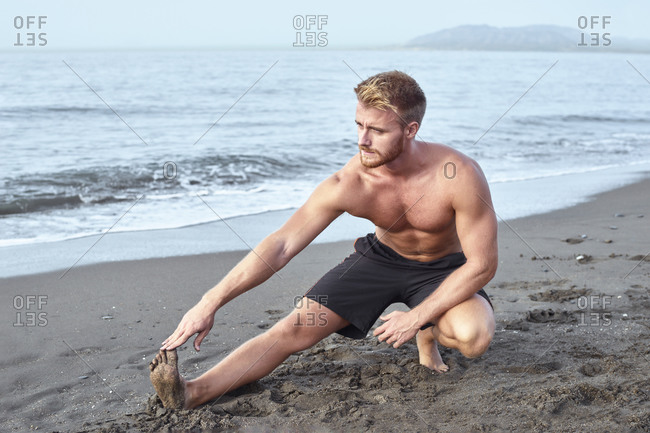 Shirtless young red-haired athlete trains on the beach