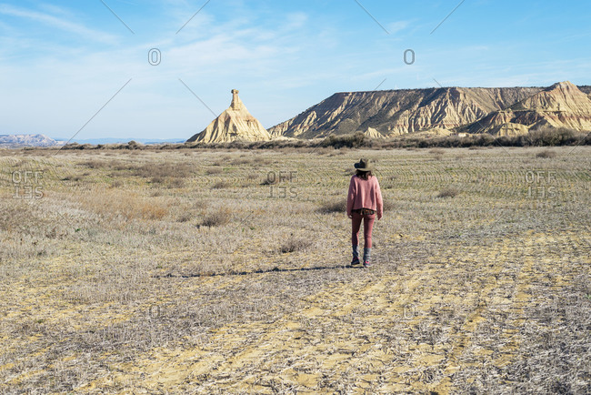 Rear view of a woman in pink clothes walking in a desert in sunny day